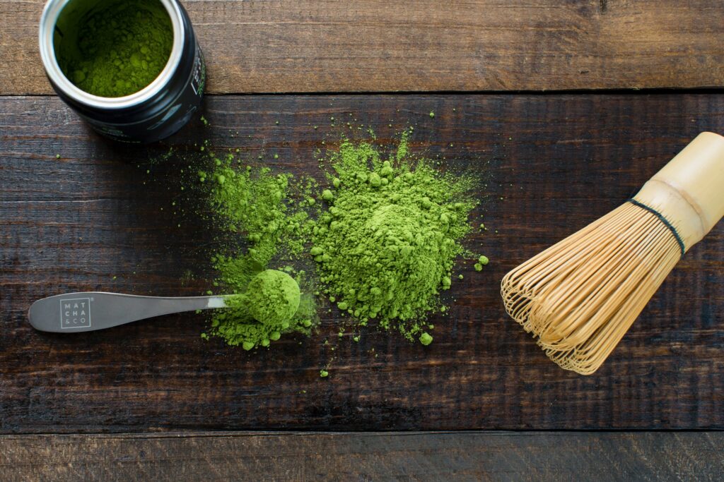木のテーブルに広がる抹茶パウダーと茶筅