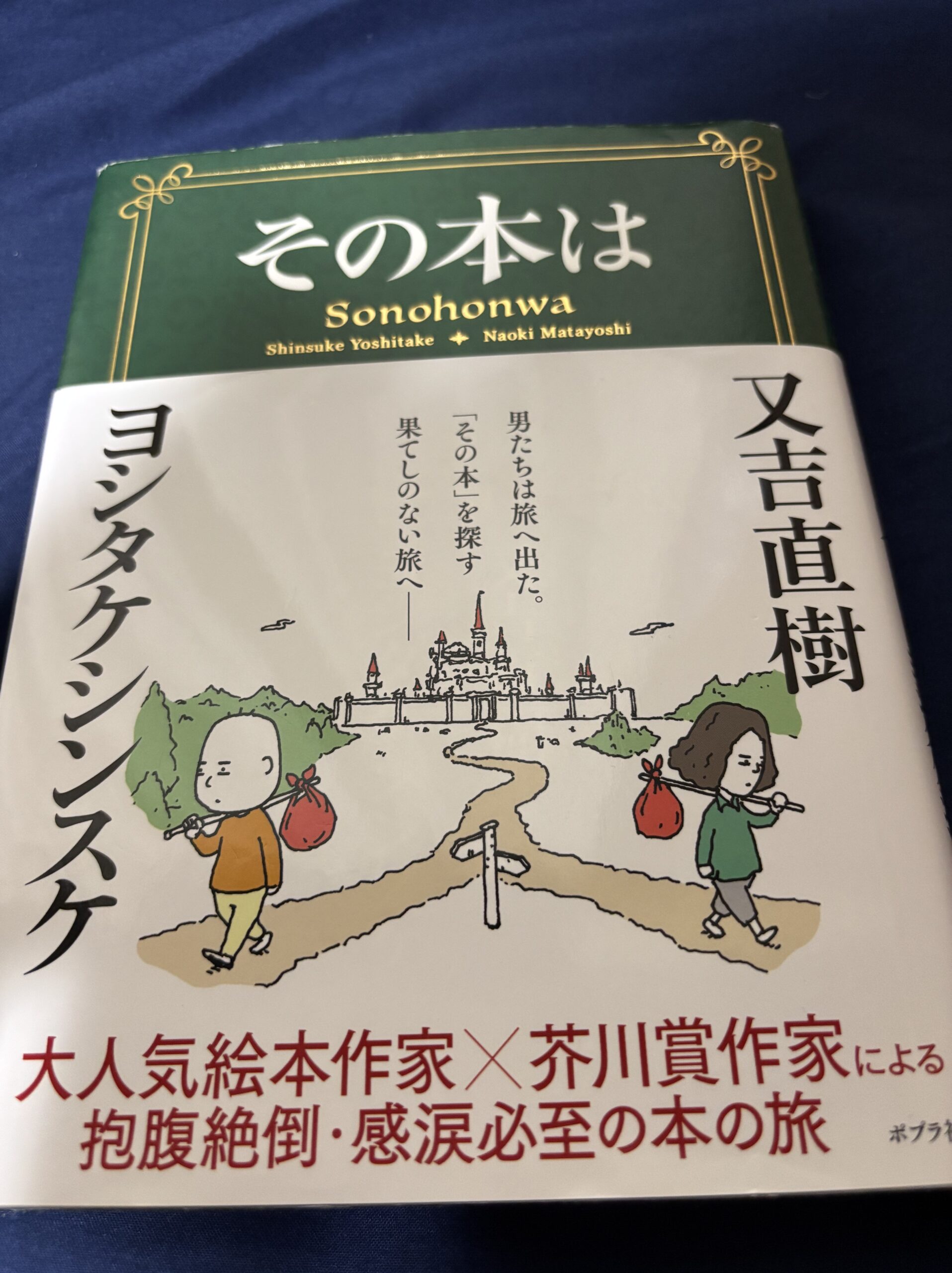 又吉直樹とヨシタケシンスケの共著「その本は」の表紙。二人の人物が風呂敷を背負って旅に出るイラスト。